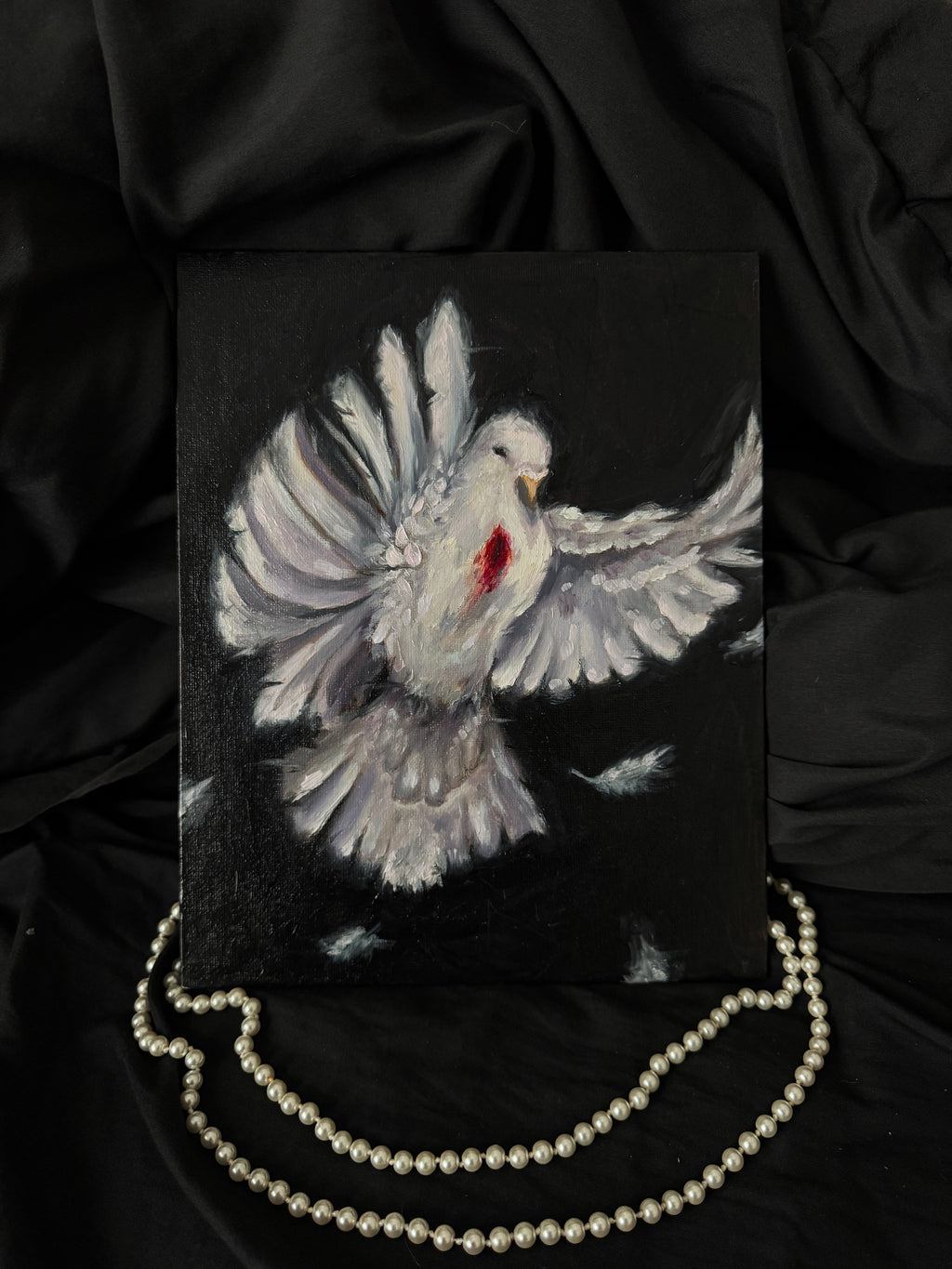 Painting of a dove with a wound on a black background, accompanied by a pearl necklace.