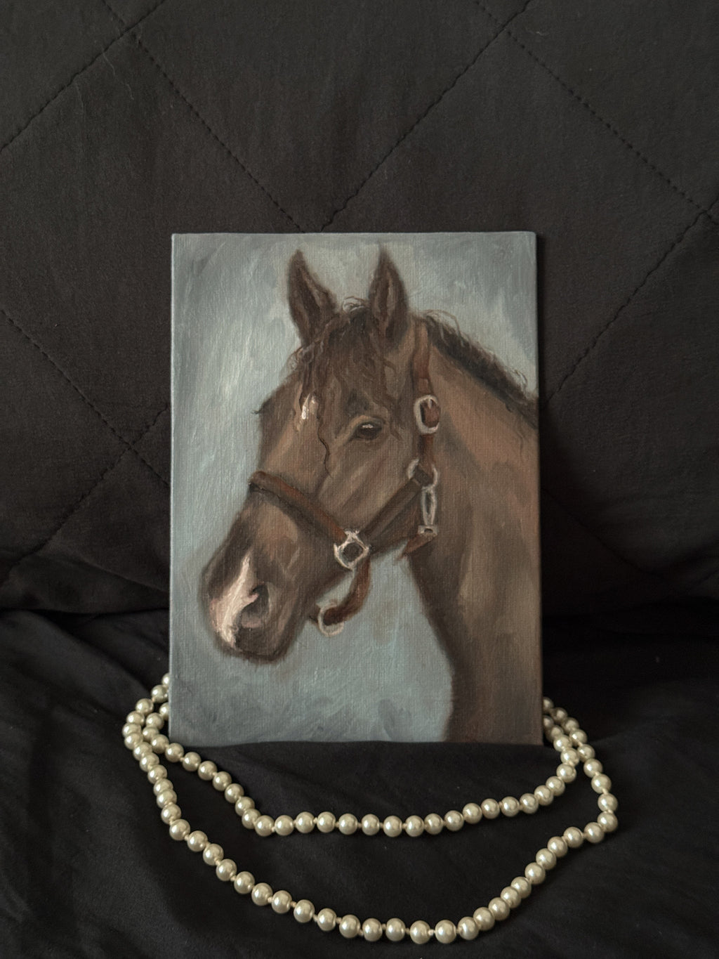 Painting of a horse with a bridle on a dark surface with pearls.