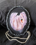 oil painting of a swan with an ornamental border with a black background, accompanied by a pearl necklace.