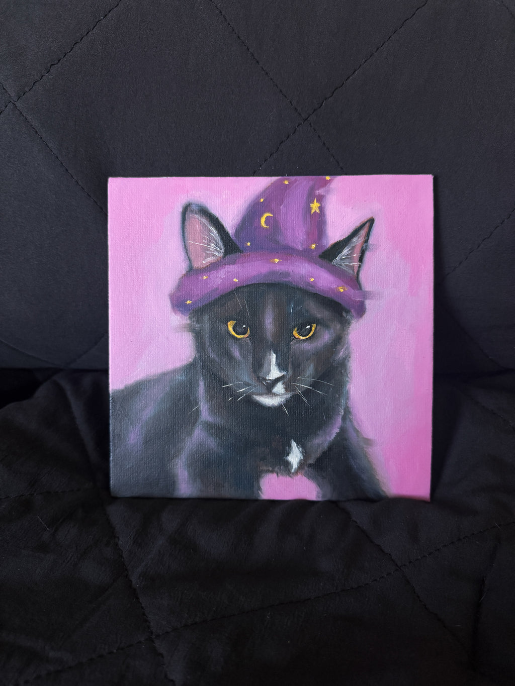 Painting of a black cat wearing a purple wizard hat on a pink background