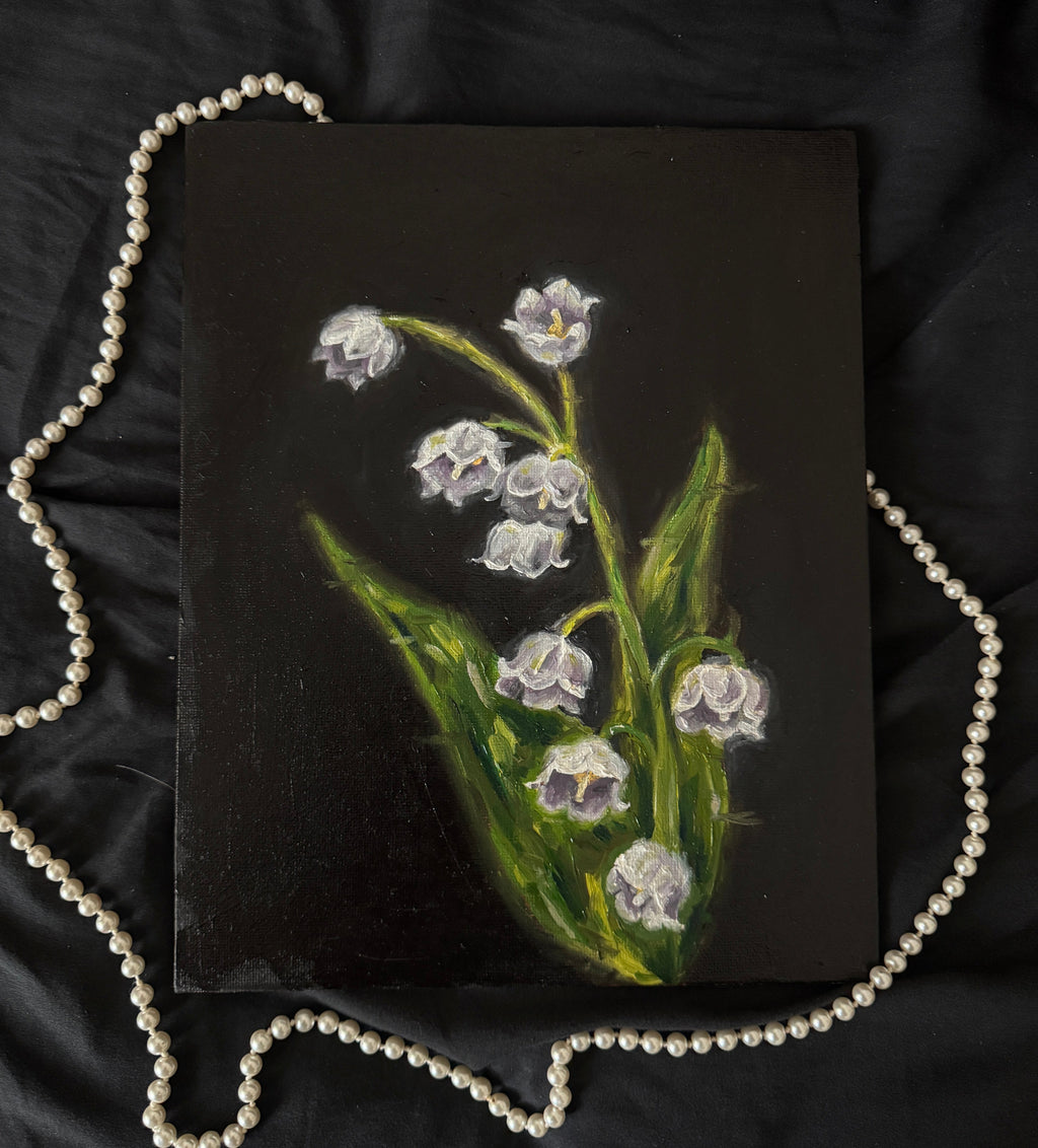 Small painting of lilies of the valley on a dark surface with a pearl necklace.