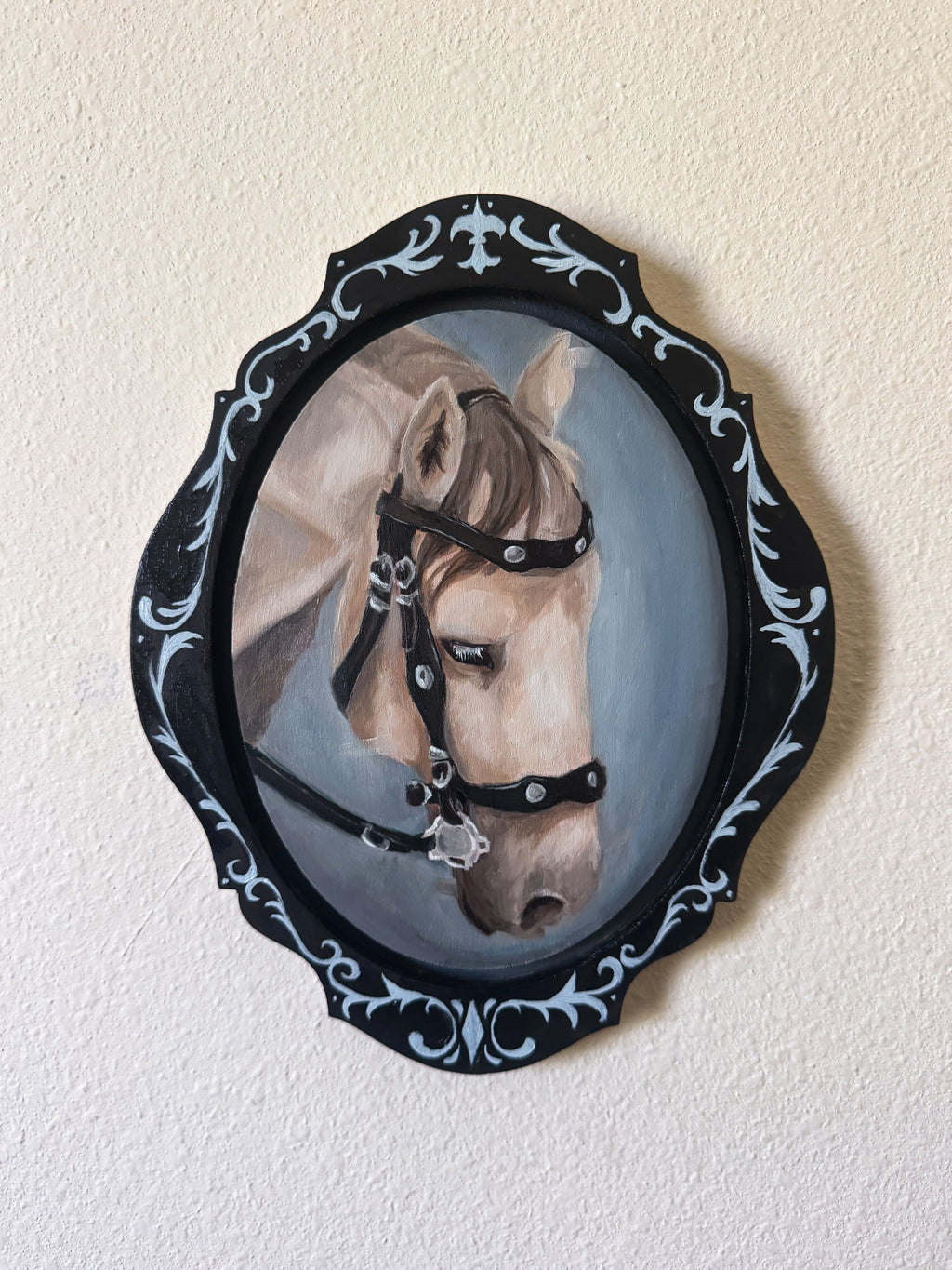 Painting of a horse's head in a decorative black frame on a beige wall.