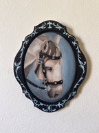 Painting of a horse's head in a decorative black frame on a beige wall.
