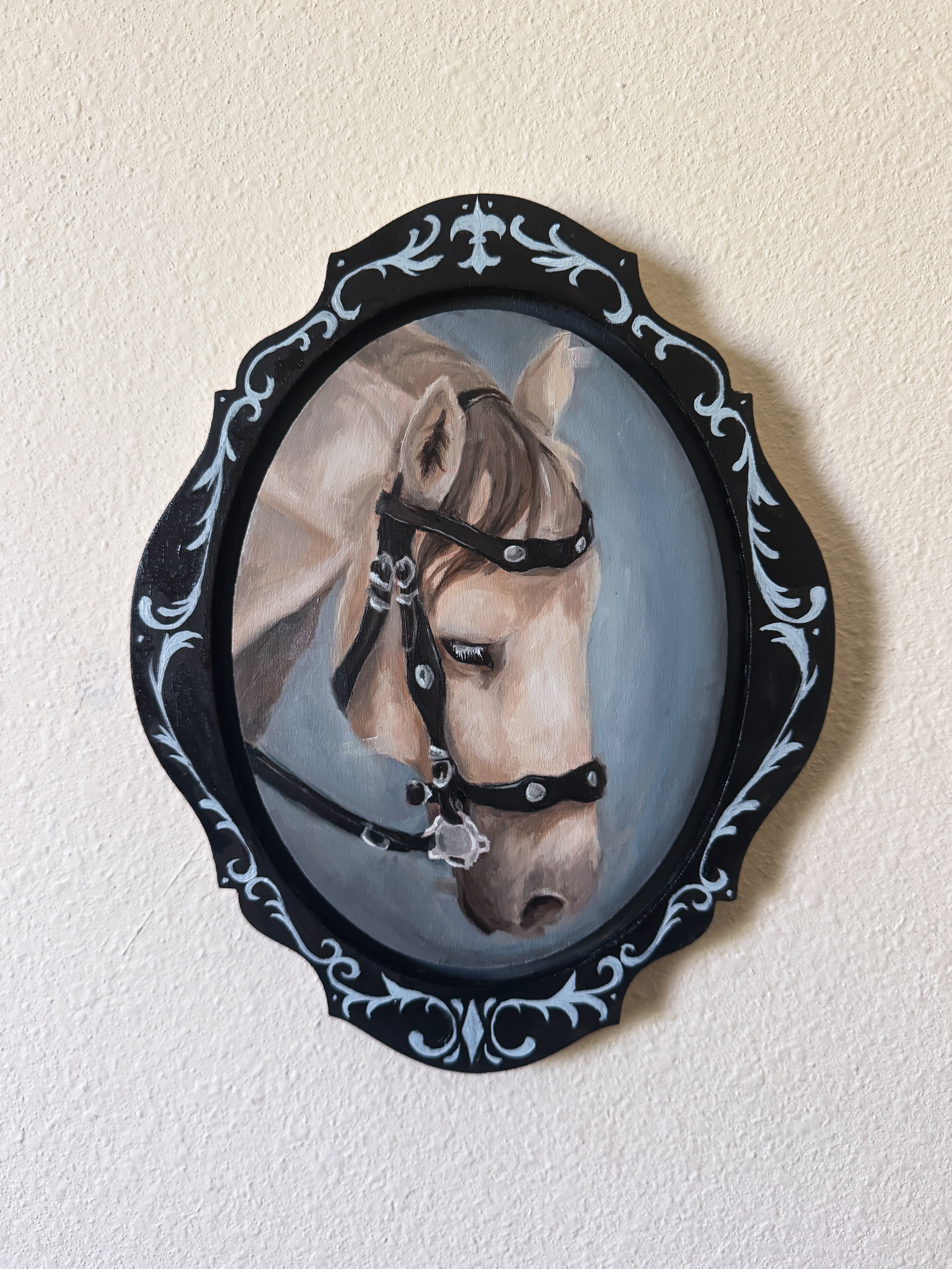 Painting of a horse's head in a decorative black frame on a beige wall.