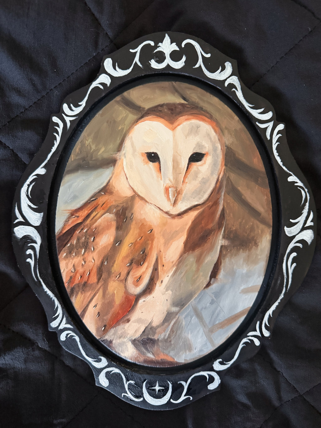 Oval painting of an owl in a decorative frame on a dark fabric background