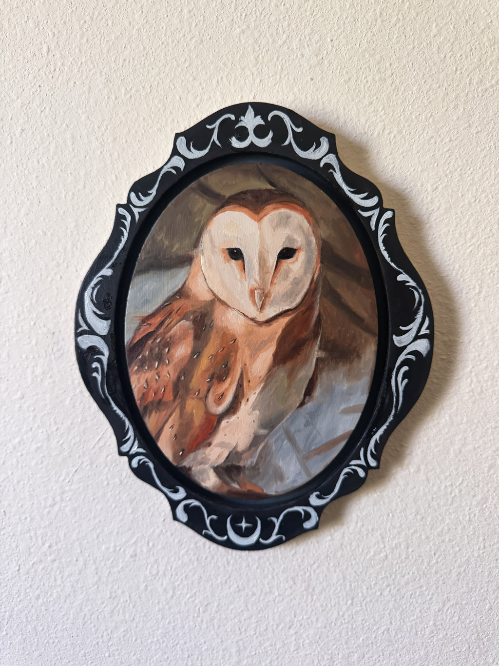 Painting of an owl in a decorative black frame on a beige wall