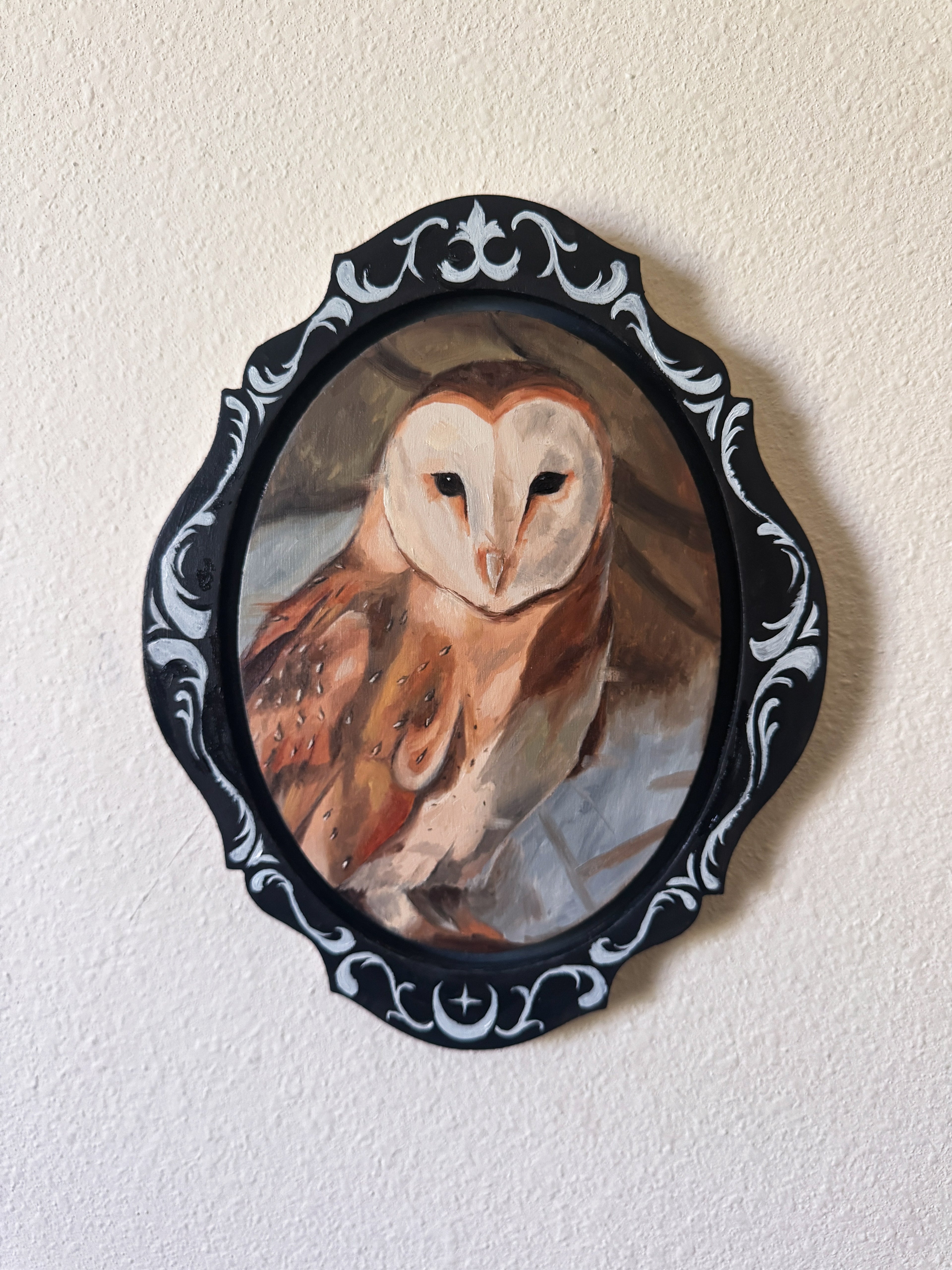 Painting of an owl in a decorative black frame on a beige wall